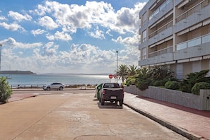 A parking area with a car and a truck, a sign indicating no parking, a building with balconies, and a view of the sea. - Oceana Suites Remanso (Punta del Este)