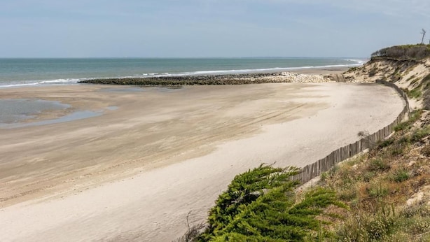Ein Strand mit Holzplanken, Felsen und vereinzelter Vegetation.