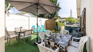 Eine Terrasse mit Tisch und Stühlen, einem großen Sonnenschirm und einem Holzzaun im Hintergrund.