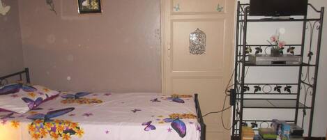 A bedroom with a bed, a TV on a shelf, and a door with a birdcage decoration.