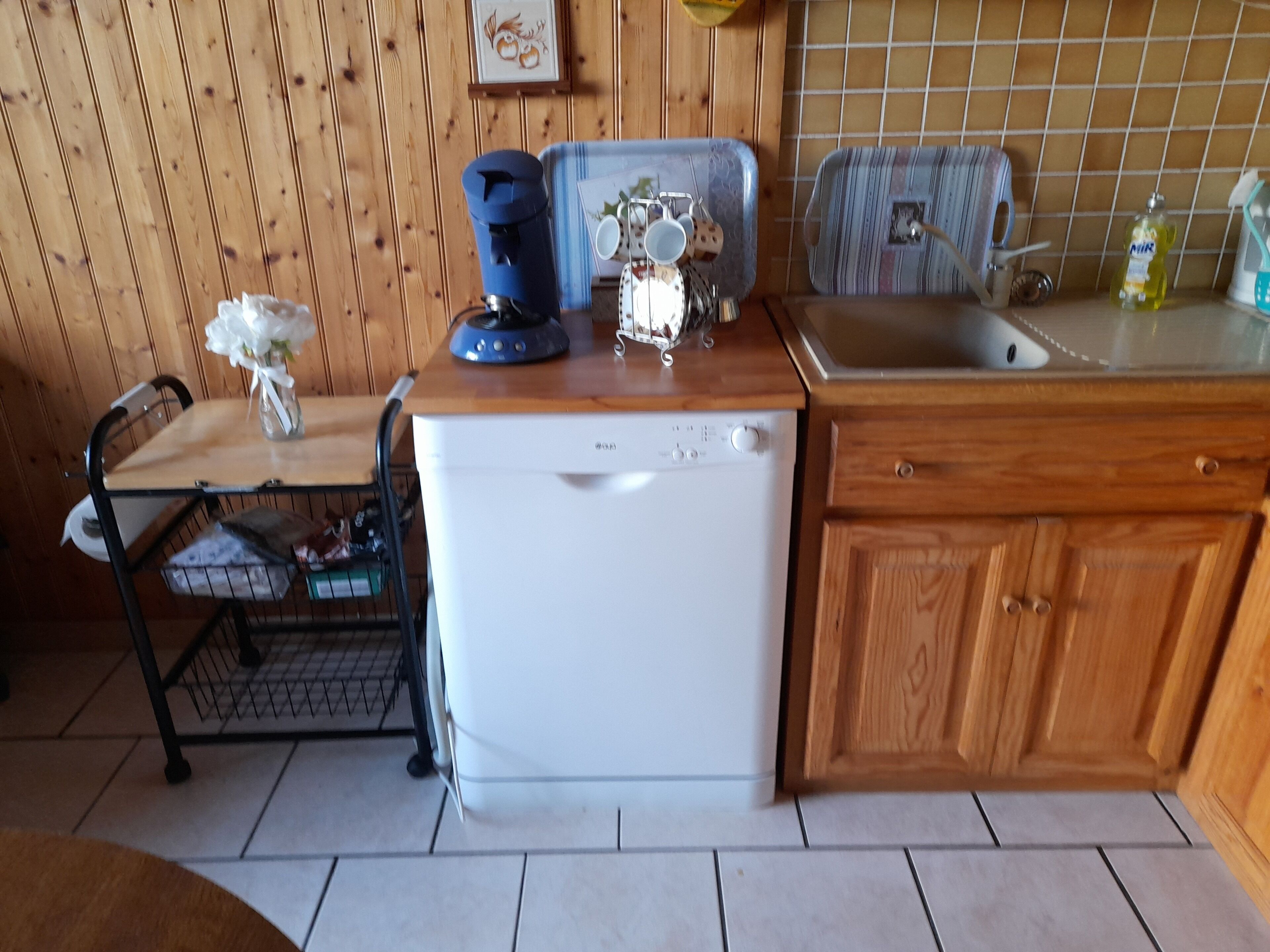 Eine kompakte Küche mit einem weißen Kühlschrank, Holzschränken, einer Spüle und einem kleinen Esstisch mit Stühlen.