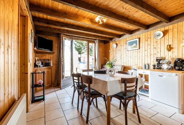 A wooden interior with a dining table and chairs, a kitchen area, and a television mounted on the wall.