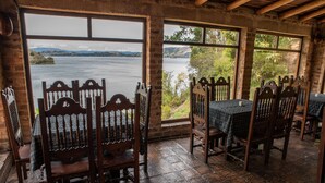 Una habitación rústica con muebles de madera, ventanas amplias con vistas a un lago y una pared de ladrillo.