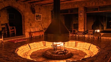 Una habitación con paredes de piedra, chimenea central, muebles de madera y suelo de piedra.