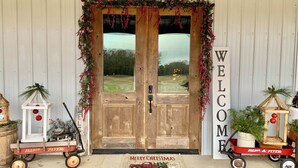 A wooden double door with a "WELCOME" sign, decorated with greenery and red ornaments, flanked by vintage red wagon-style mailboxes.