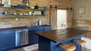 A rustic kitchen with wooden walls, a stainless steel dishwasher, a wooden bar counter with stools, and a sign reading "FRESH EGGS".