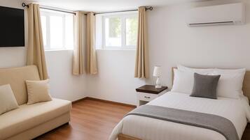 Une chambre d’hôtel équipée d’un lit, d’un canapé, d’une table de chevet avec une lampe et d’un appareil de climatisation.