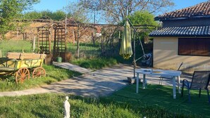 Un espacio al aire libre rústico con un carro de madera, un paraguas verde y una pequeña mesa con sillas.