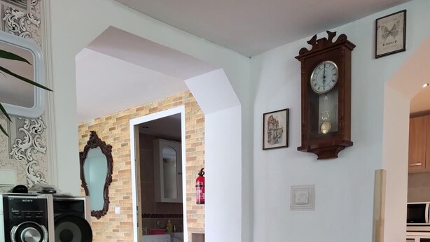 Un salón con suelo de madera, un mueble de entretenimiento negro, un tapete rosa y una mesa de comedor con un plato rojo.