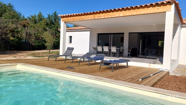 Un área de piscina moderna al aire libre con sillones de descanso y una terraza de madera.