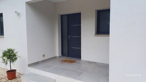 Una entrada moderna con una puerta azul oscuro, una planta en maceta y una ventana pequeña.