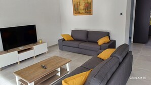 Una sala de estar moderna con un televisor de pantalla plana, un sofá gris con cojines amarillos, una mesa de centro de madera y un cuadro en la pared.
