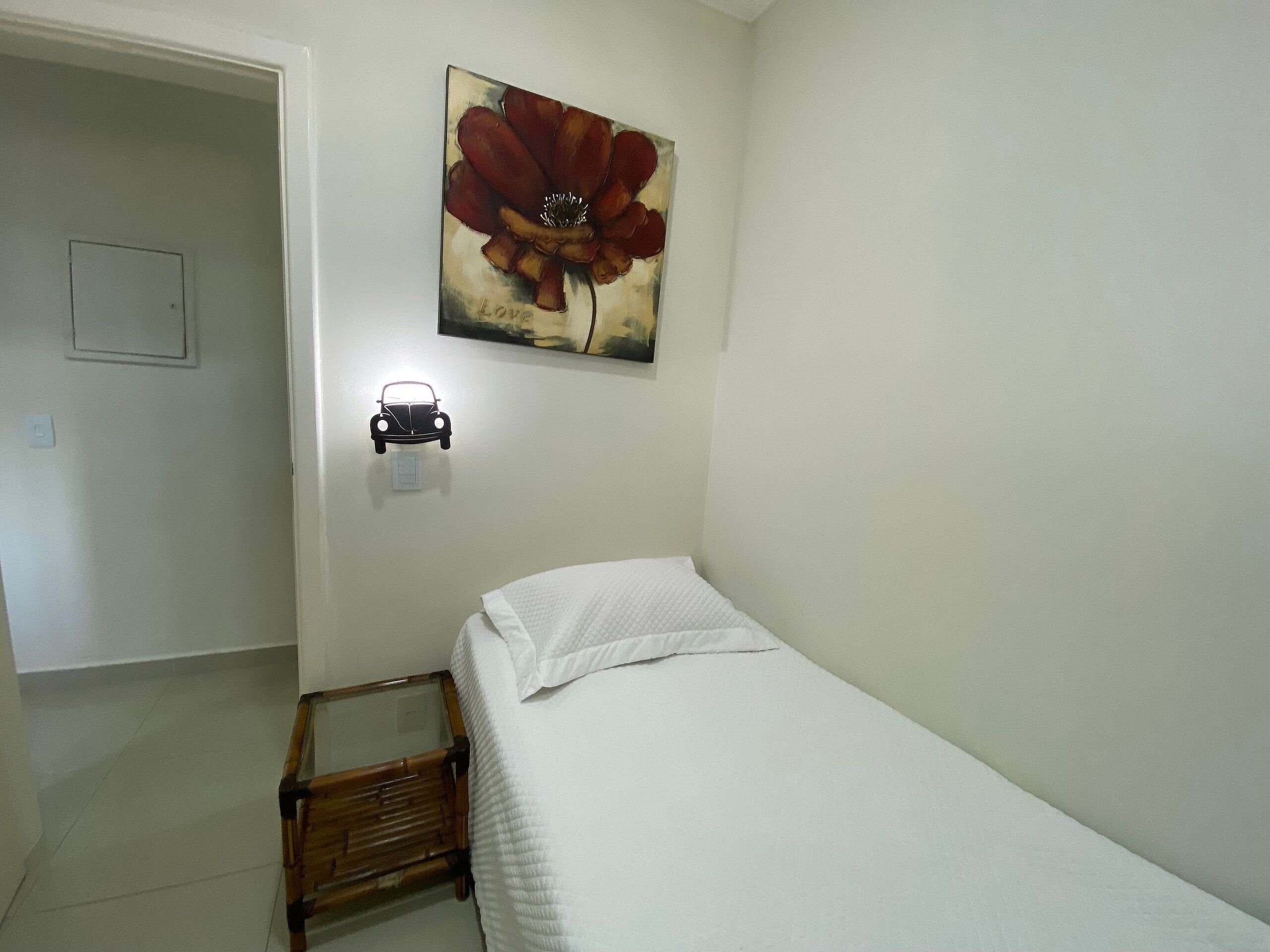 Ein Schlafzimmer mit einem Bett, einem Holzstuhl, einer Wandleuchte und einem Blumenbild.