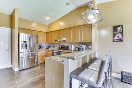 A kitchen with wooden cabinets, stainless steel appliances, a granite countertop, and a bar area with leather stools.. Near Beaches: Pet-Friendly Sunrise Escape w/ Patio