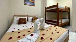 A hotel room with a bed adorned with rose petals and a towel shaped like a heart. There is a bunk bed to the right and a painting on the wall. - Pousada Mar Suites (Ubatuba)