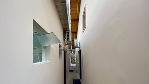 A narrow hallway with a glass window on the left, a vent on the right, and a blue mat on the floor. - Pousada Mar Suites (Ubatuba)