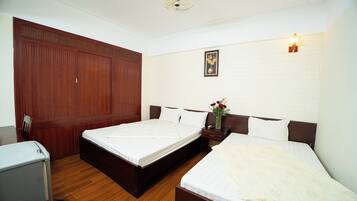 A room with two beds, a wooden wardrobe, a desk, and a small table with a vase of flowers.