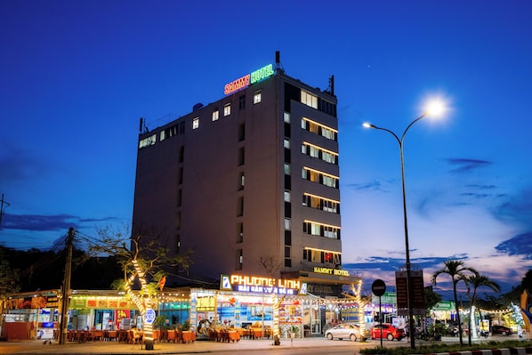 Un hôtel à plusieurs étages, avec une enseigne indiquant « SAMMY HOTEL » et un restaurant appelé « PHOENIX LUNA » à l’avant.