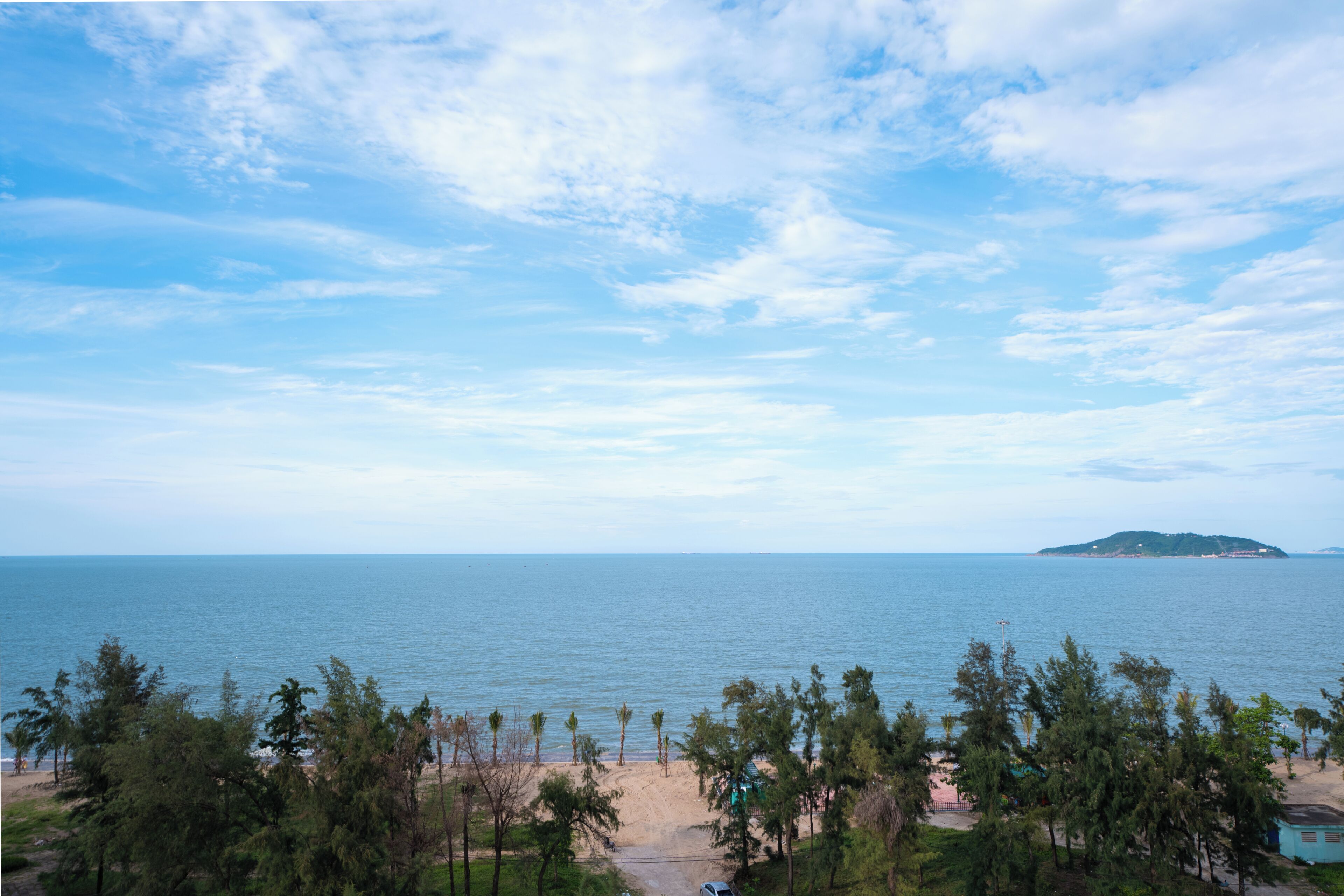 A beach view with a clear sky, a sandy beach, and a small island in the distance.