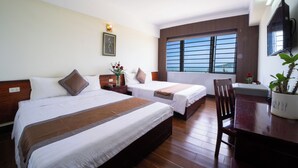 Habitación de hotel con dos camas, un escritorio de madera, una silla, un televisor, una ventana con persianas y un ventilador de techo.