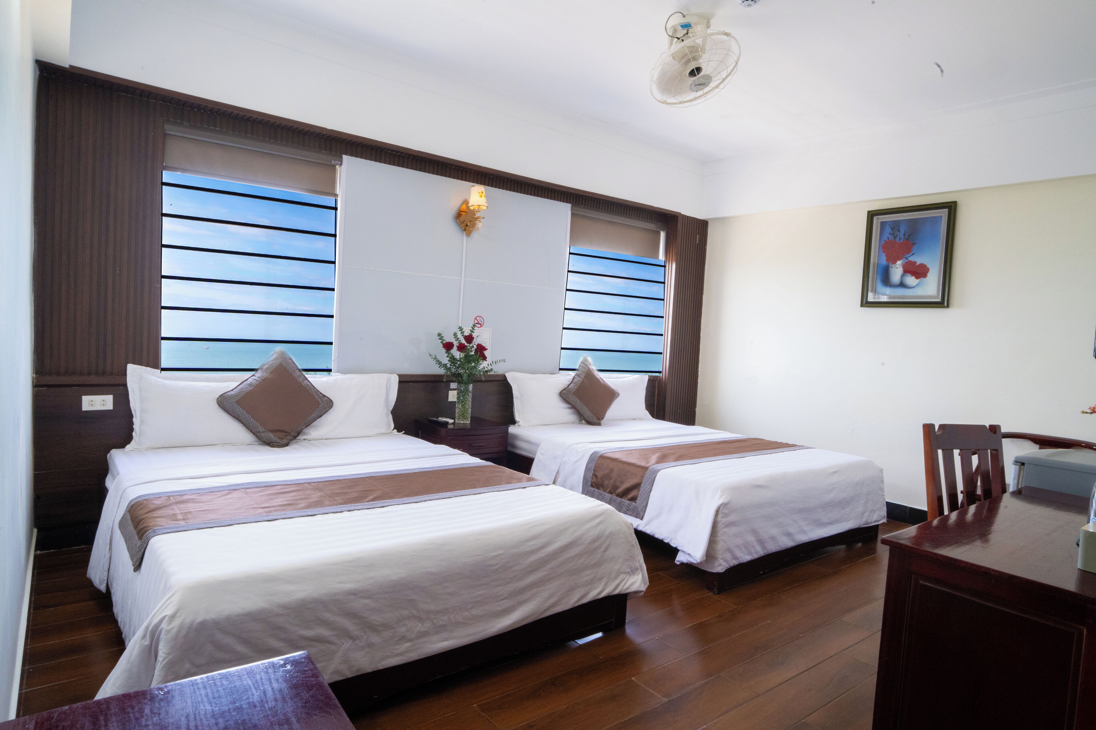 A hotel room with two beds, a desk, a chair, a nightstand, and a window with blinds.