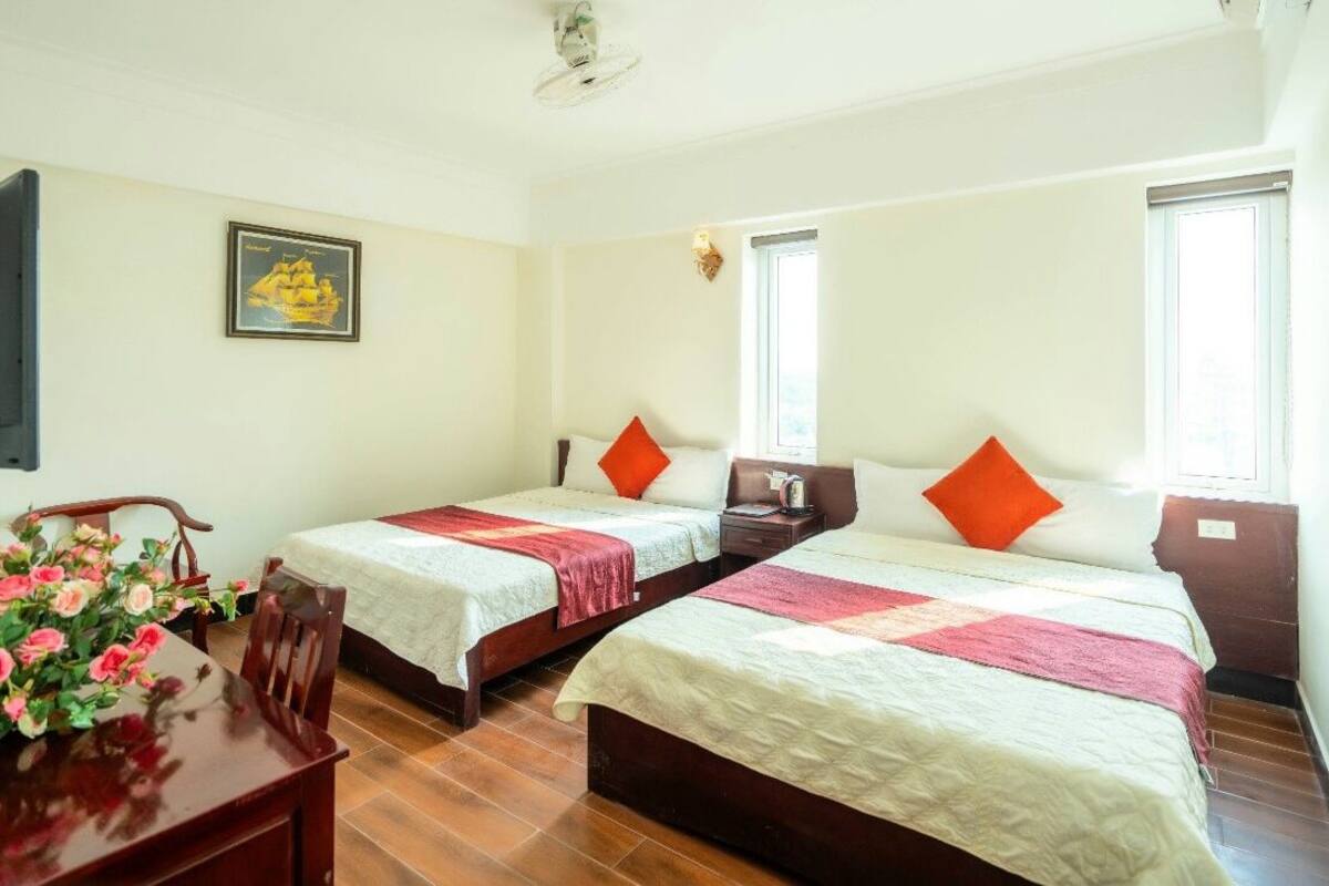 A room with two beds, a wooden table with a vase of flowers, and a framed picture on the wall.