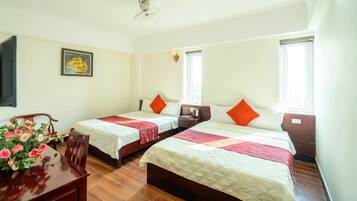 Ein Zimmer mit zwei Betten, einem Holztisch mit Blumenvase und einem gerahmten Bild an der Wand.