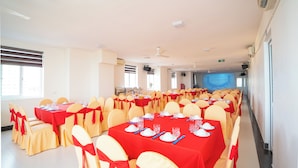 Un salón de banquetes con varias mesas, sillas y una pantalla de proyección.