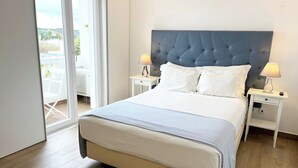 Ein ordentlich eingerichtetes Schlafzimmer mit einem großen Bett, zwei Nachttischen mit Lampen und einer Schiebetür zu einem Außenbereich.