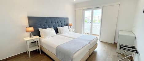 A modern hotel room with a large bed, two bedside tables, and a view of the outside through a sliding door.