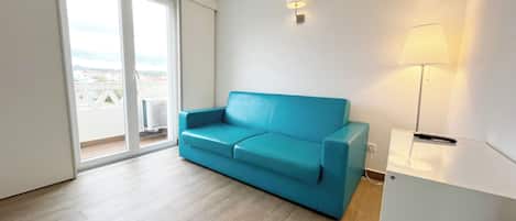 A room with a blue sofa, a standing lamp, and a sliding glass door leading to an outdoor area.
