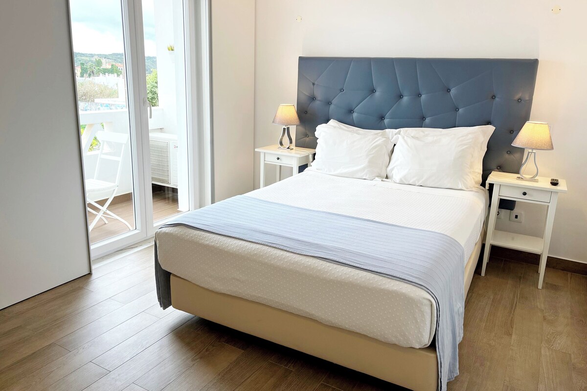 A neatly arranged bedroom with a large bed, two bedside tables with lamps, and a sliding glass door leading to an outdoor area.