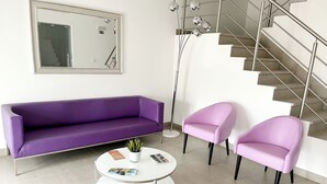Ein modernes Wohnzimmer mit einem violetten Sofa, zwei rosafarbenen Sesseln und einem weißen Couchtisch mit Zeitschriften.