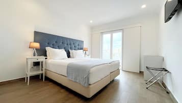 A modern bedroom with a large bed, white nightstands, and a flat-screen TV mounted on the wall.