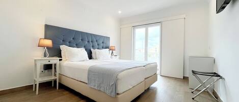 Un dormitorio moderno con una cama grande, mesitas de noche blancas y un televisor de pantalla plana montado en la pared.
