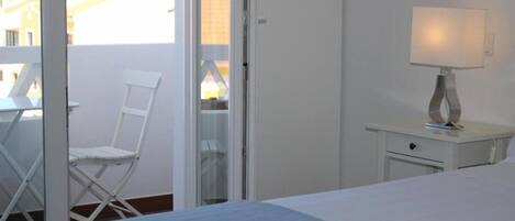 Et hotelværelse med en seng, en stol, et natbord med lampe og en skydedør til et udendørs område.