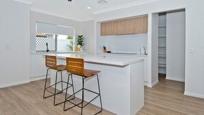 A modern kitchen with a white island, two wooden bar stools, a wooden cabinet above the island, and a glass door leading to a balcony. - Freedom Beach Homes Unit 199B Brand New in Rainbow Bay with private plunge pool and Wi-Fi Inc. (Coolangatta)