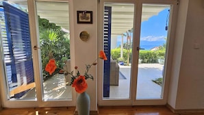 A room with a wooden floor, a vase with flowers, and a view through glass doors to an outdoor area with greenery and a clear sky. - Holiday apartment with terrace and sea view (Njivice)