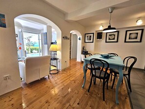 Uma área de refeições com mesa azul e cadeiras pretas, luminária amarela e quadros nas paredes.