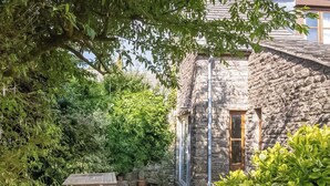 A stone building with a wooden door and a window, surrounded by lush greenery and a stone bench. - 2 bedroom accommodation in Acton (Acton)