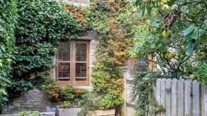 A stone building with a wooden window, surrounded by lush greenery and a wooden fence. - 2 bedroom accommodation in Acton (Acton)