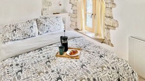 A cozy bedroom with a stone wall, a bed with patterned bedding, a bedside table with a lamp, and a window with curtains. - 2 bedroom accommodation in Acton (Acton)