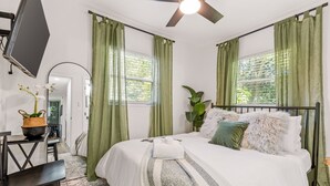 A bedroom with a bed, a desk, a chair, a TV, and a ceiling fan.