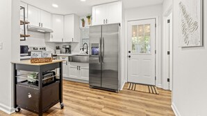 A modern kitchen with white cabinets, a stainless steel refrigerator, and a wooden floor.