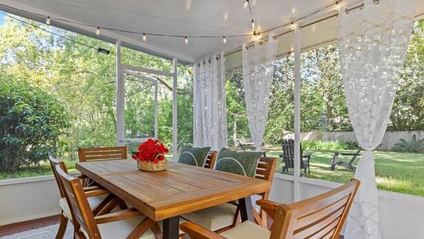A wooden dining table with chairs, a basket of flowers, and a view of a garden through large windows.