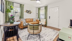 A living room with a sofa, a round table, a wicker chair, a ceiling fan, and a green curtain.