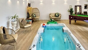 A room with a hot tub, lounge chairs, a pool table, and a potted plant.
