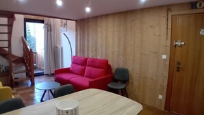 Una sala de estar con un sofá rojo, una mesa de comedor y una escalera que sube a otro nivel.