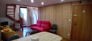 Uma sala de estar com um sofá vermelho, uma mesa de jantar e uma escada que leva a outro andar.