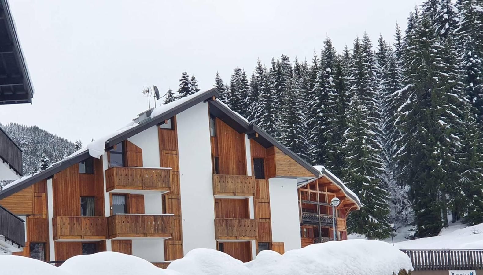 A multi-story wooden building with balconies, surrounded by snow-covered trees.